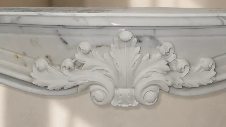 L'immagine mostra da vicino la fascia scolpita di un caminetto in marmo bianco