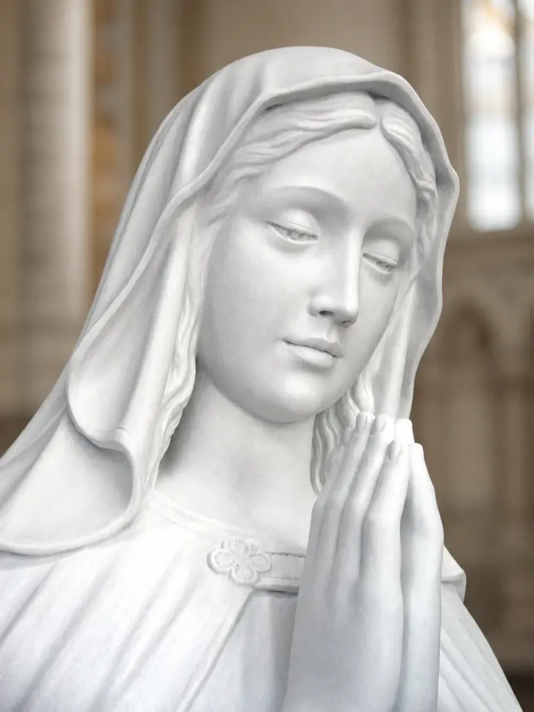 Particolare di madonna in preghiera in marmo bianco, con primo piano del volto velato e delle mani unite