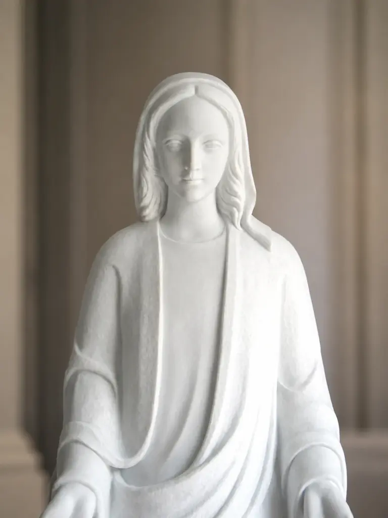 Particolare di madonna in marmo bianco, con figura frontale velata con braccia aperte e veste dalle linee essenziali