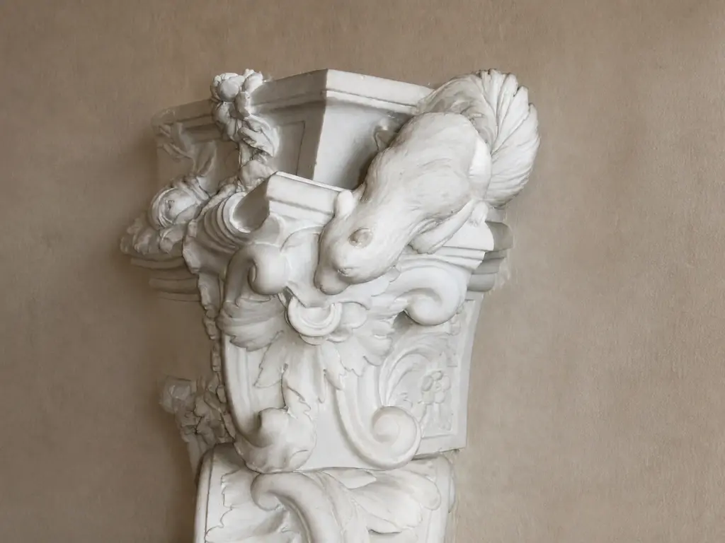 L'immagine evidenzia un elemento laterale del caminetto rococò, composto da una figura scolpita, un cartiglio e volute sovrapposte