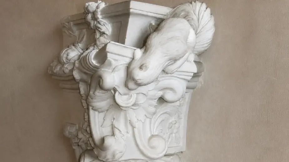 L'immagine evidenzia un elemento laterale del caminetto rococò, composto da una figura scolpita, un cartiglio e volute sovrapposte